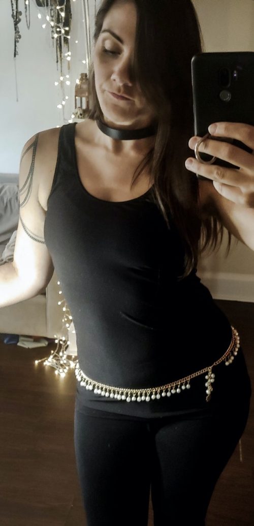 Selfie of a person with dark hair and a black outfit with a custom bellybelt with drop chains in gold.