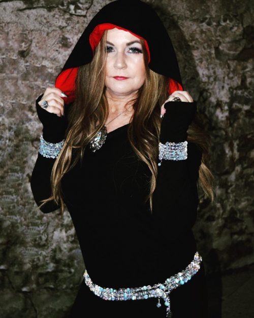 Leann wearing a black hooded outfit with a thick crystal bellybelt around their hip with three rows of crystal beads.