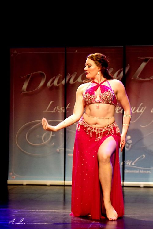 Bellydancer on stage in a red outfit wearing a bellybelt while dancing.