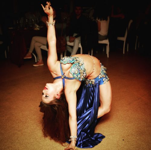 Dancer bending backward in a blue intricate outfit wearing a bellybelt.
