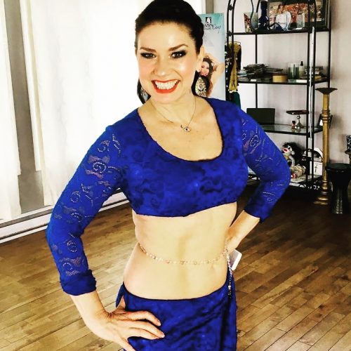 Customer smiling with their hands on their waist in a blue bellydance outfit and a white and gold bellybelt.