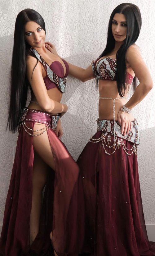 Two bellydancers in matching burgundy outfits and wearing clear beaded bellybelts.