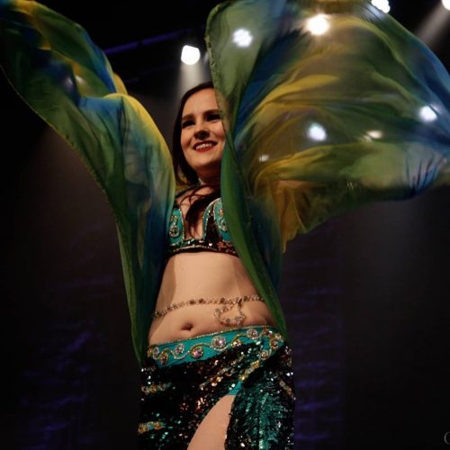 Bellydancer dancing in a green outfit with a colourful shawl wearing a gold and custom beaded bellybelt.