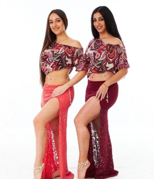 Two dancers posing in matching outfits wearing long drop chain bellybelts.