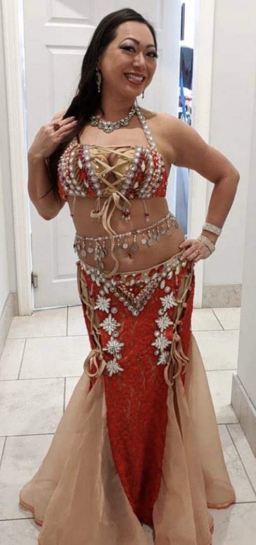 Bellydancer posing in a glimmery red outfit wearing a bellybelt with large dangling pendents.
