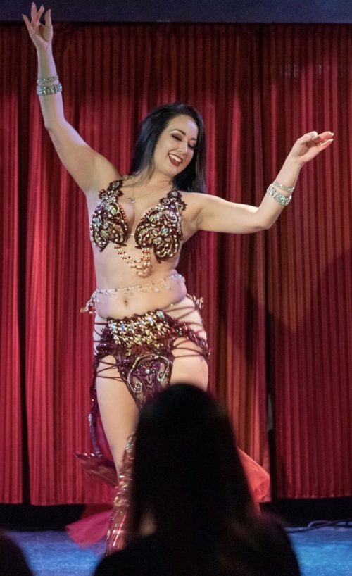 Dancer on stage in a deep maroon and glittery outfit wearing a bellybelt with clear beads and drop down pendents.