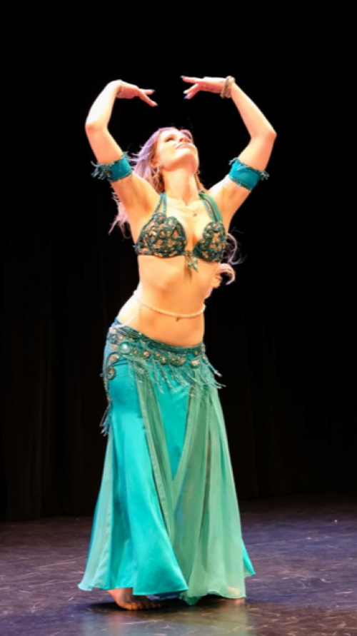 Bellydancer in an aqua outfit on stage dancing while wearing a bellybelt.