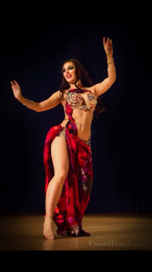 Dancer on stage wearing a red outfit wearing a clear beaded bellybelt.