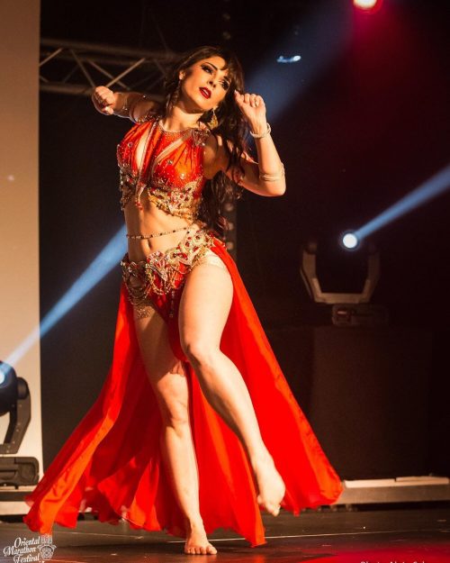 Bellydancer dancing in a red outfit on stage while wearing a custom gold beaded bellybelt.