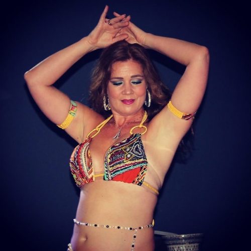 Dancer with their arms in the air in a multicolour outfit wearing a clear and dark gem bellybelt.