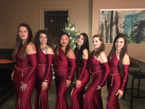 Group photo of six bellydancers wearing satin maroon dresses and bellybelts on top in gold.