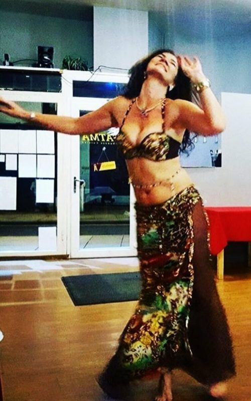 Customer dancing in a dark and colourful outfit while wearing a gold and dark beaded bellybelt.